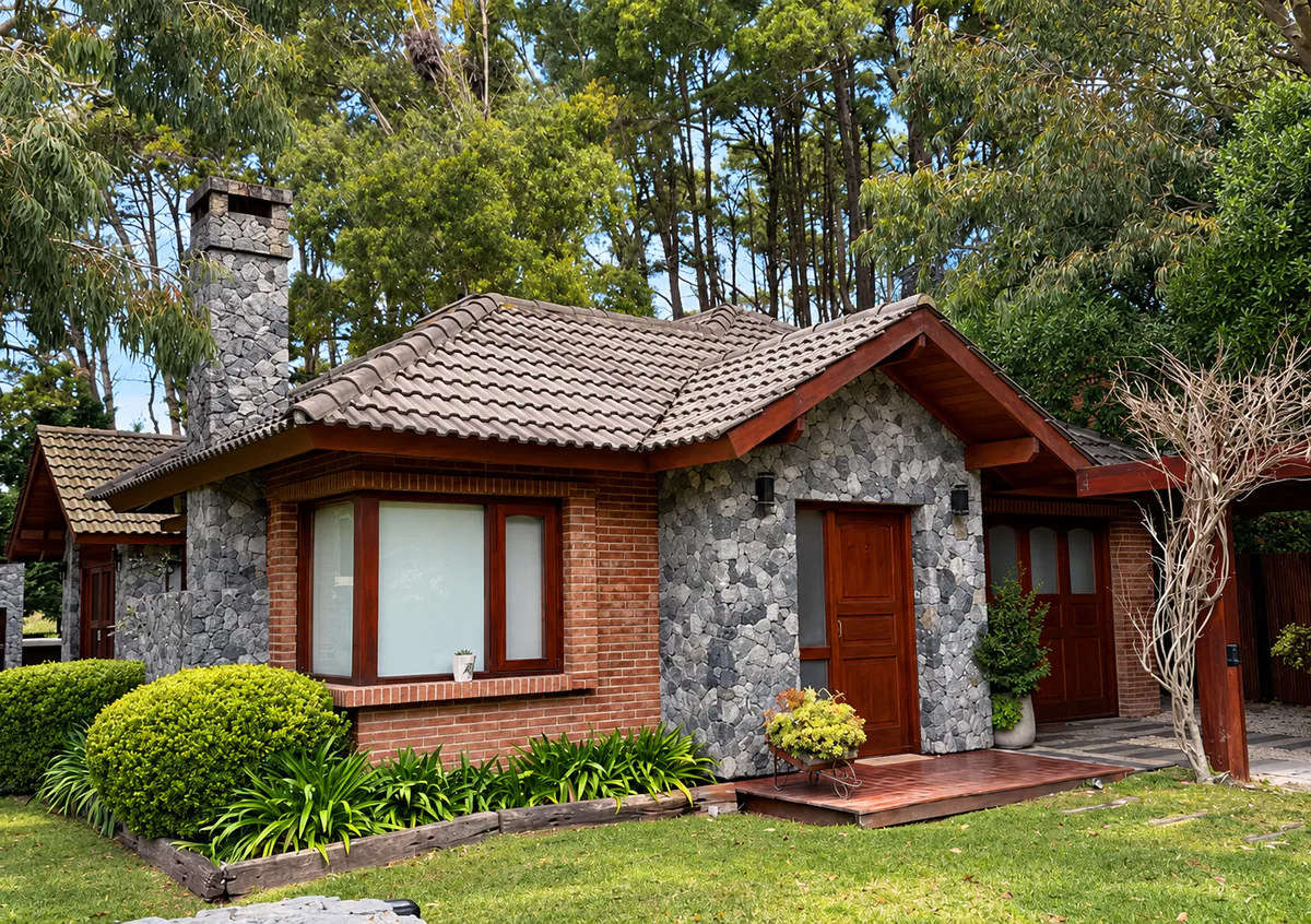 Frente de vivienda de piedra, ladrillo y madera rodeada por un jardín.
