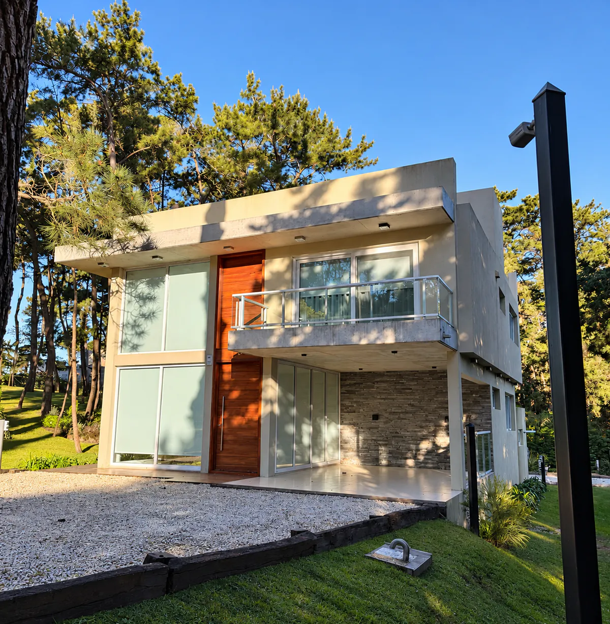 Frente de vivienda contemporánea de dos plantas entre pinos.